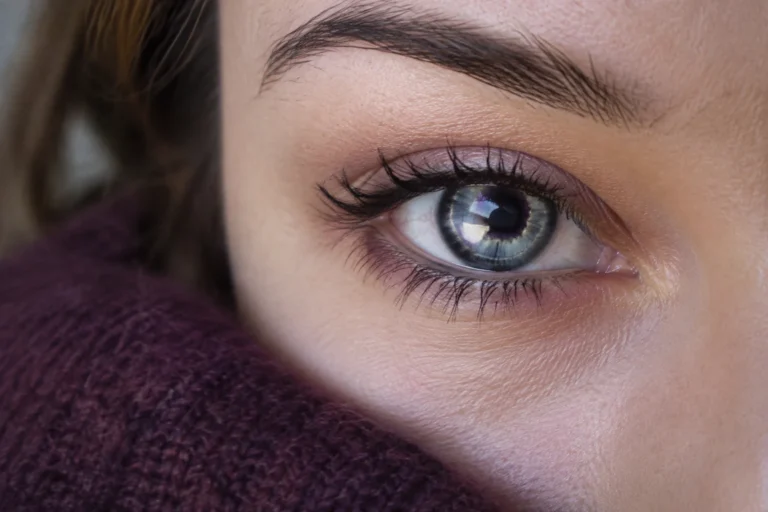 Gros plan sur un œil bleu-gris très clair aux reflets violacés, éclairé par une lumière douce